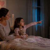Parent sitting calmly beside a child in bed as the child points toward something unseen in the room, representing children sensing ghosts, energy, or intuitive phenomena.